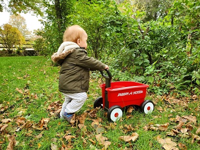 child pushing a walker red wagon in his backyard
